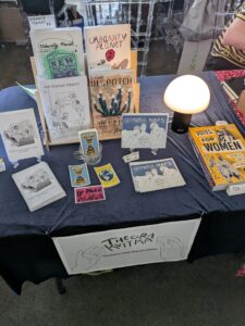 Photo of the books on Theora's table at CAKE, with the new mushroom lamp.
